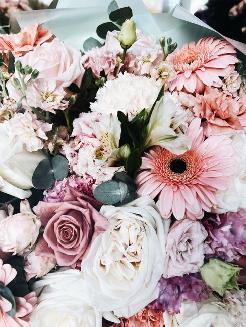 A close-up of a bouquet featuring a variety of fresh flowers including large pink gerbera daisies with dark centers, pale pink roses with tightly coiled petals, white lisianthus, light pink carnations