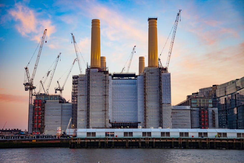 A historic power station under construction at Battersea, featuring four tall, yellow-painted chimney stacks, with several construction cranes positioned around the building. The building's exterior i